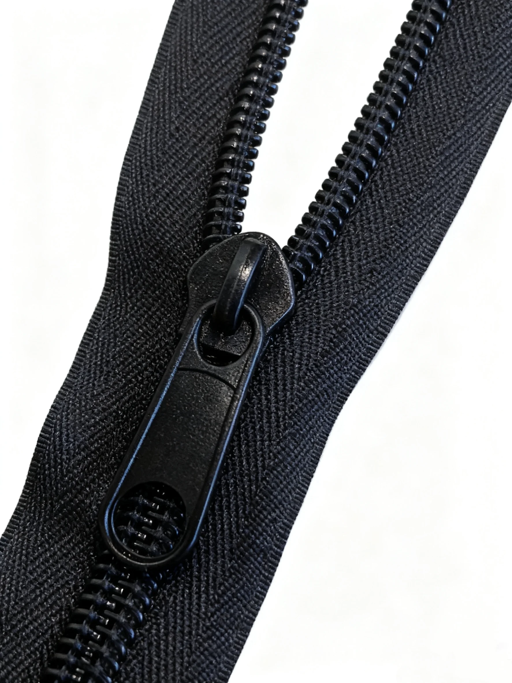 Close-up of a black nylon zipper with interlocking teeth and pull tab on textured fabric.