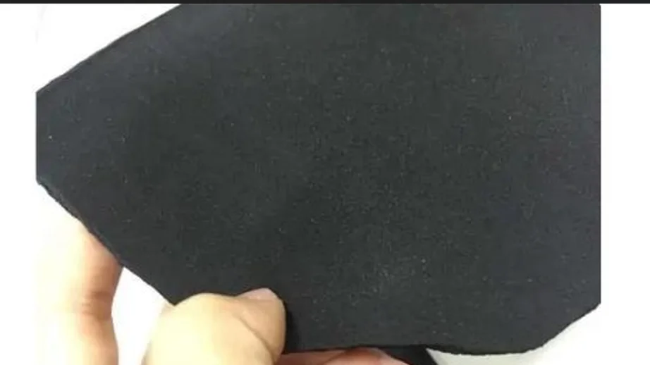 A hand holding a square black textile swatch, showcasing its texture and color, used for garment accessories.