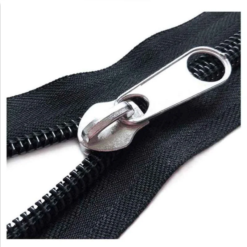 A close-up image showing a black zipper with a shiny metal slider, showcasing its teeth and fabric, laid out on a flat surface.