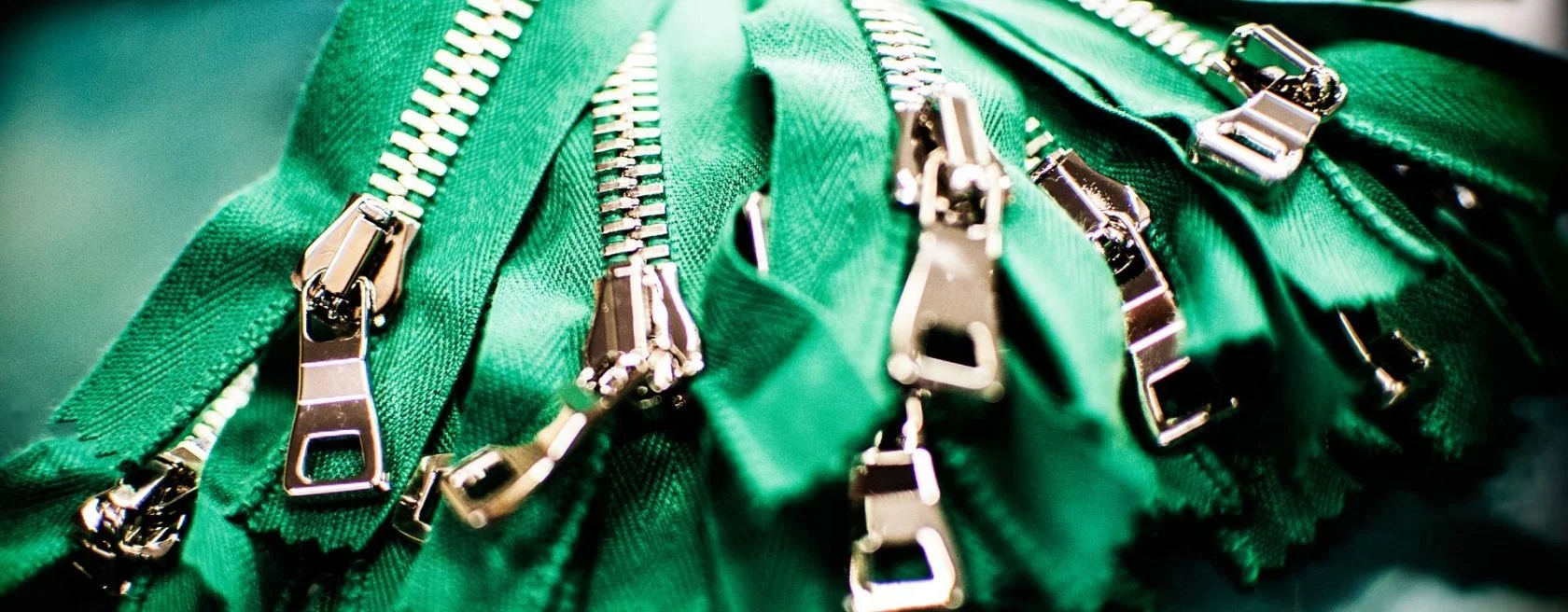 Close-up view of several green zippers with shiny metal sliders, showcasing detailed stitching and the fabric texture.