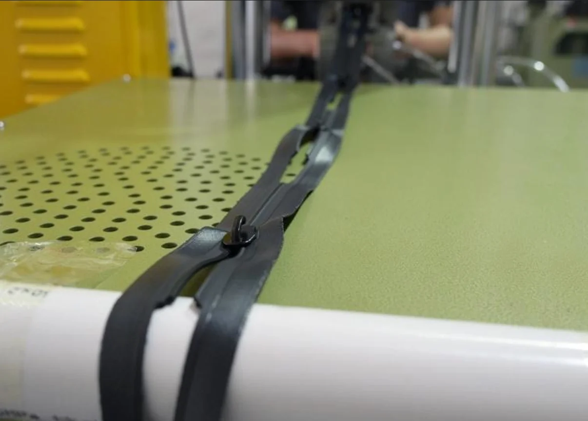 Close-up of an industrial machine sealing a black zipper on a green surface, highlighting the precision and machinery of the process.