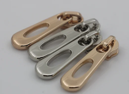 Four metal zipper pull tabs in shiny silver and gold finishes displayed on a plain surface.