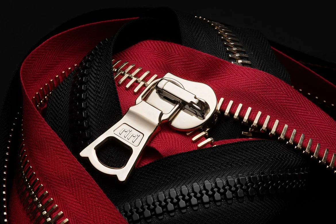 Close-up of high-quality metallic and plastic zippers on intertwined red and black tapes, showcasing premium garment accessory design.