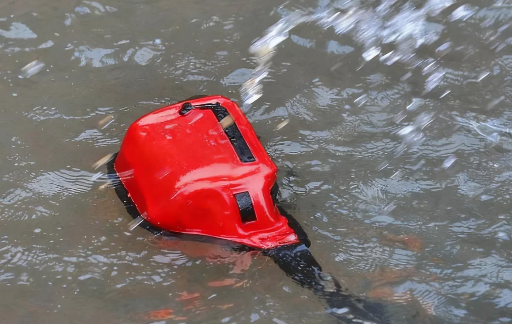 Red life jacket with black straps partially submerged and floating on water, indicating an emergency or water activity scenario.