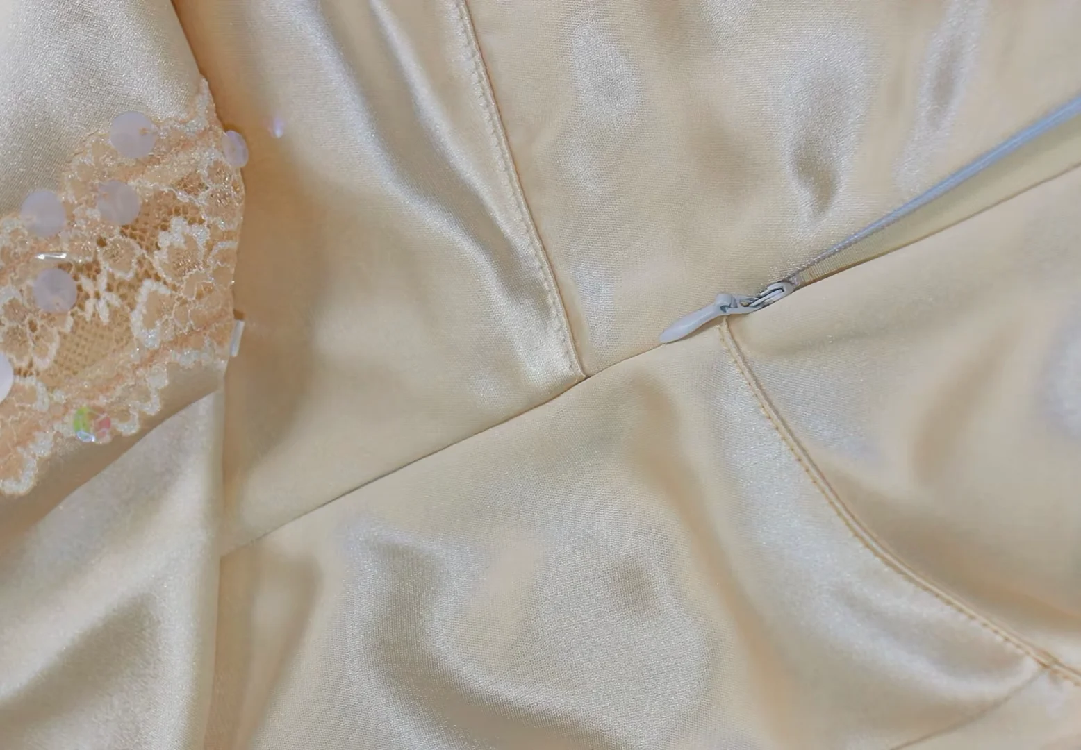 Close-up of a beige satin dress with intricate lace and sequin detailing, featuring a zipper closure.