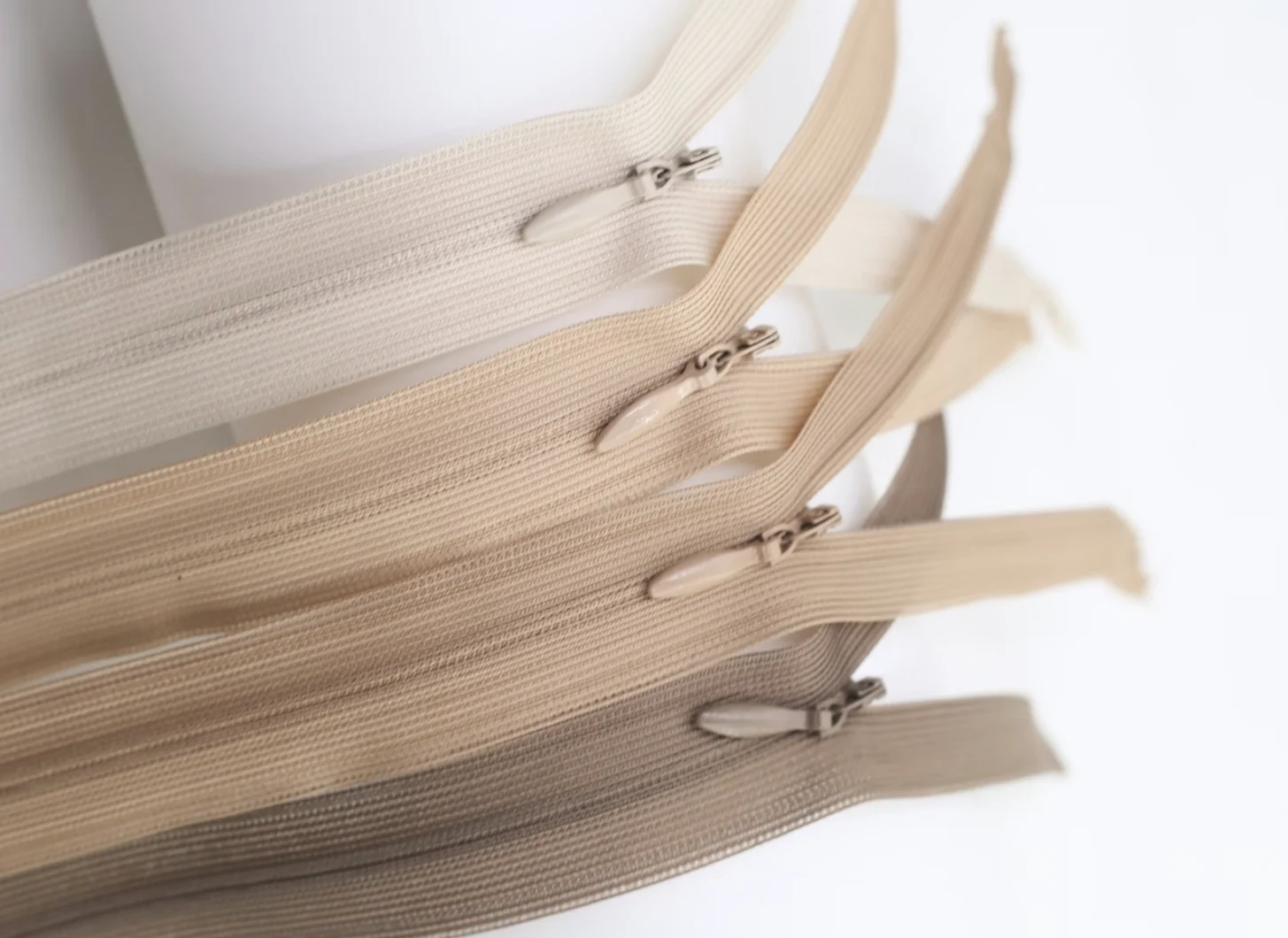 A selection of zippers in various beige tones displayed on a white background, showcasing different shades and textures.