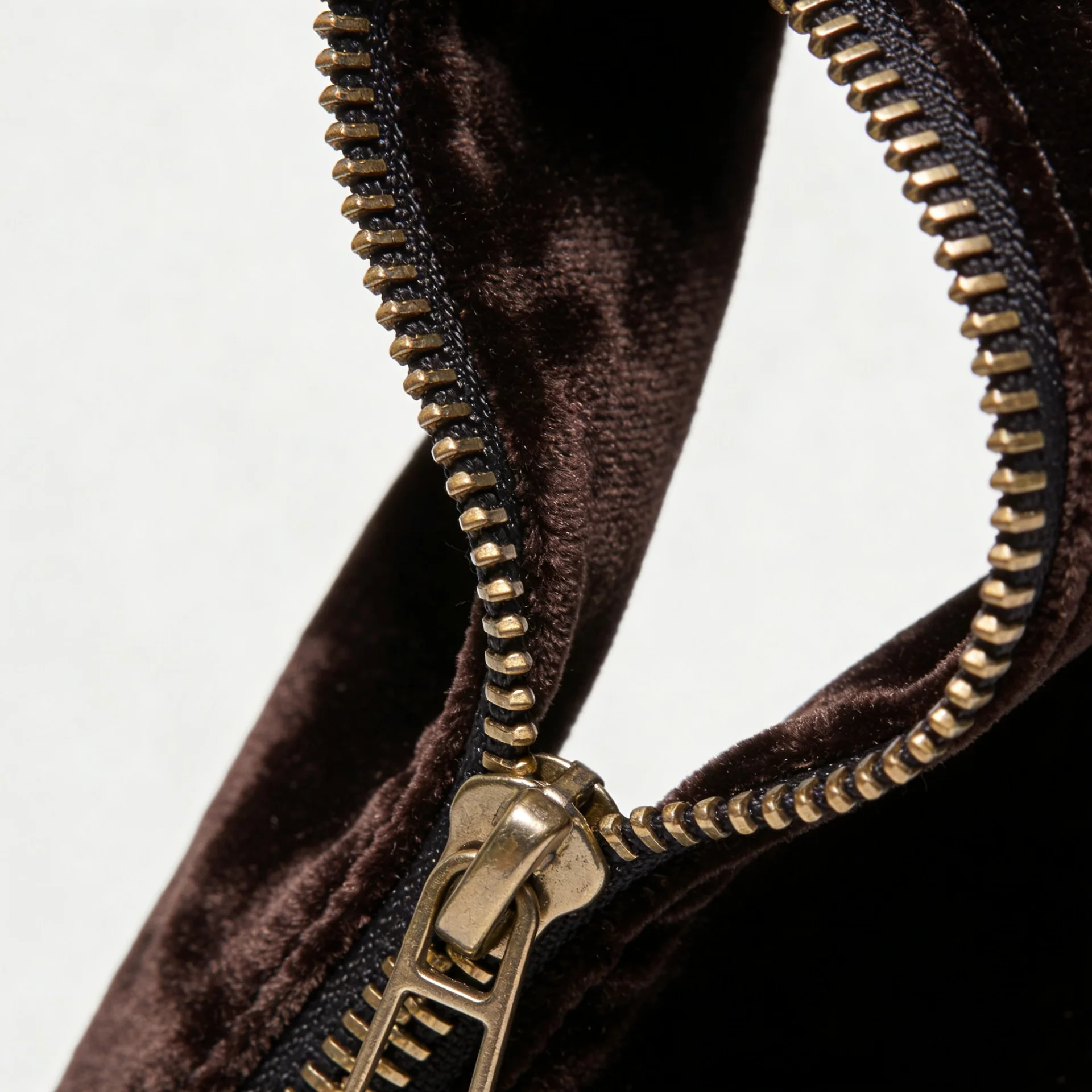 Close-up view of a gold metal zipper attached to a brown fabric, showcasing texture and detail.