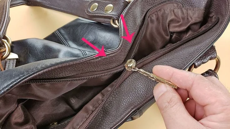 Person using a tool to repair the zipper of a brown leather bag, with arrows pointing to the zipper area.