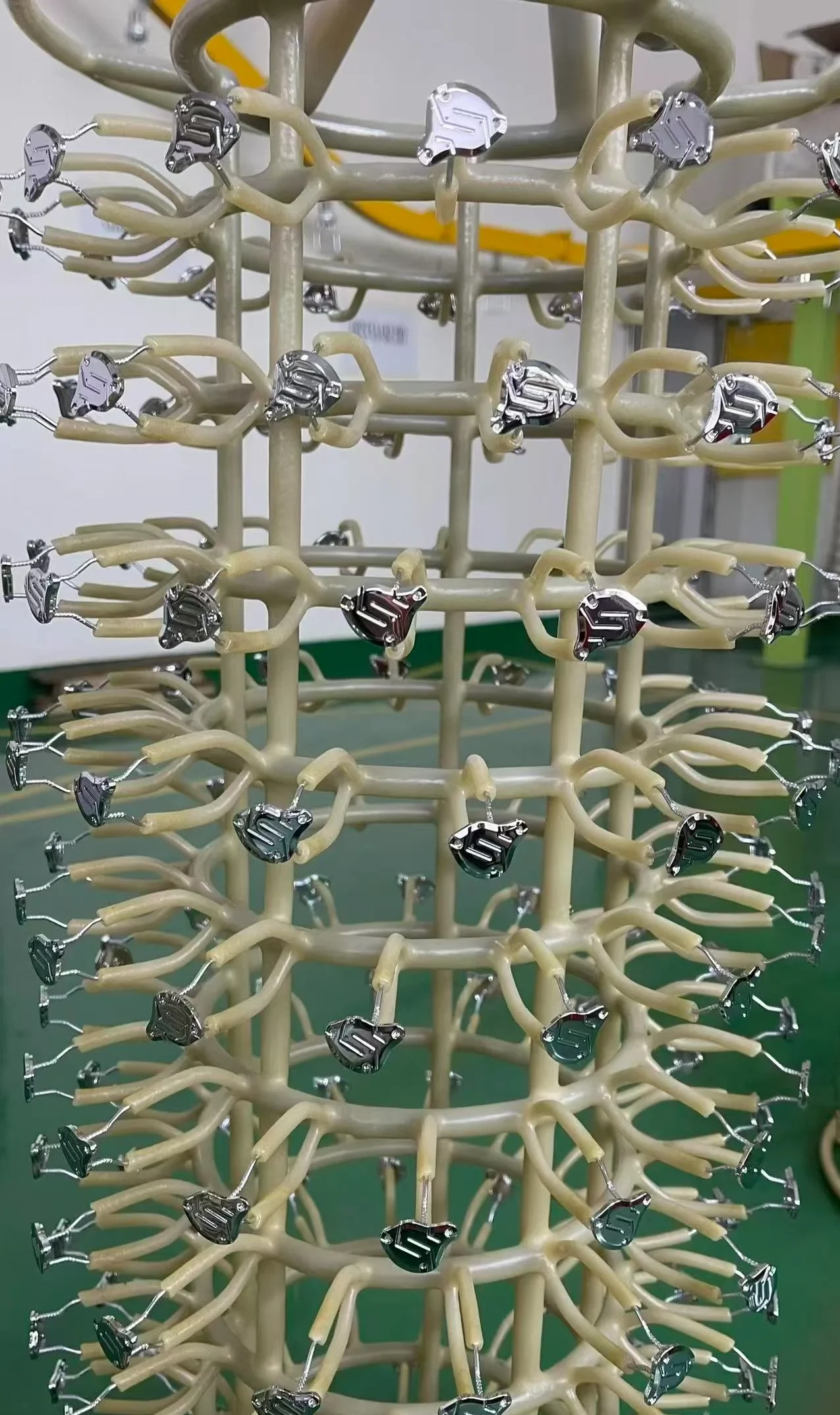 Multiple chrome metallic zippers mounted on a rotating beige rack in a manufacturing setting, showcasing intricate design and arrangement.