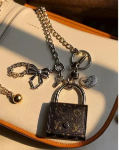 Close-up of a designer bag adorned with decorative metal charms, including a mini lock design and various shapes on a chain.