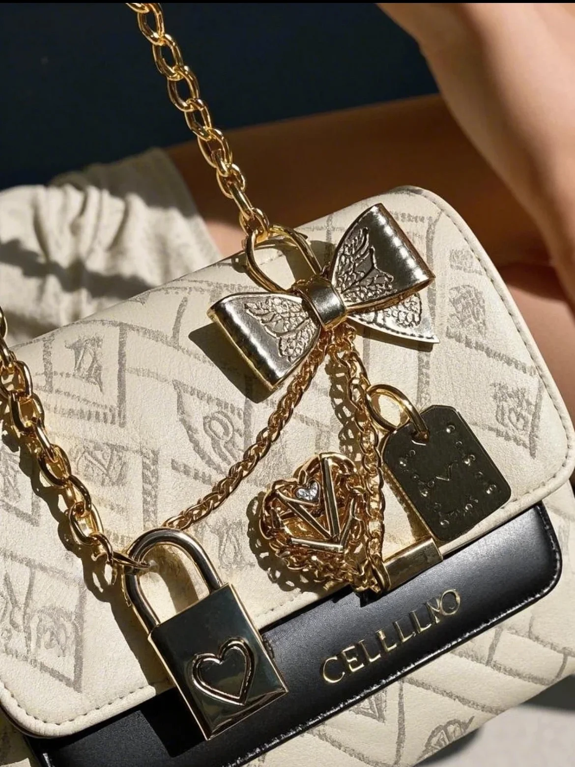 Close-up of a cream and black designer handbag adorned with gold charms, including a lock, heart, and bow with a gold chain strap.