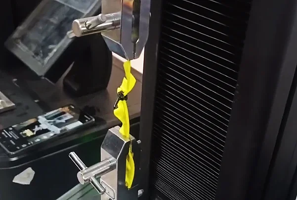 A fabric tensile testing machine gripping yellow fabric to measure strength and durability.