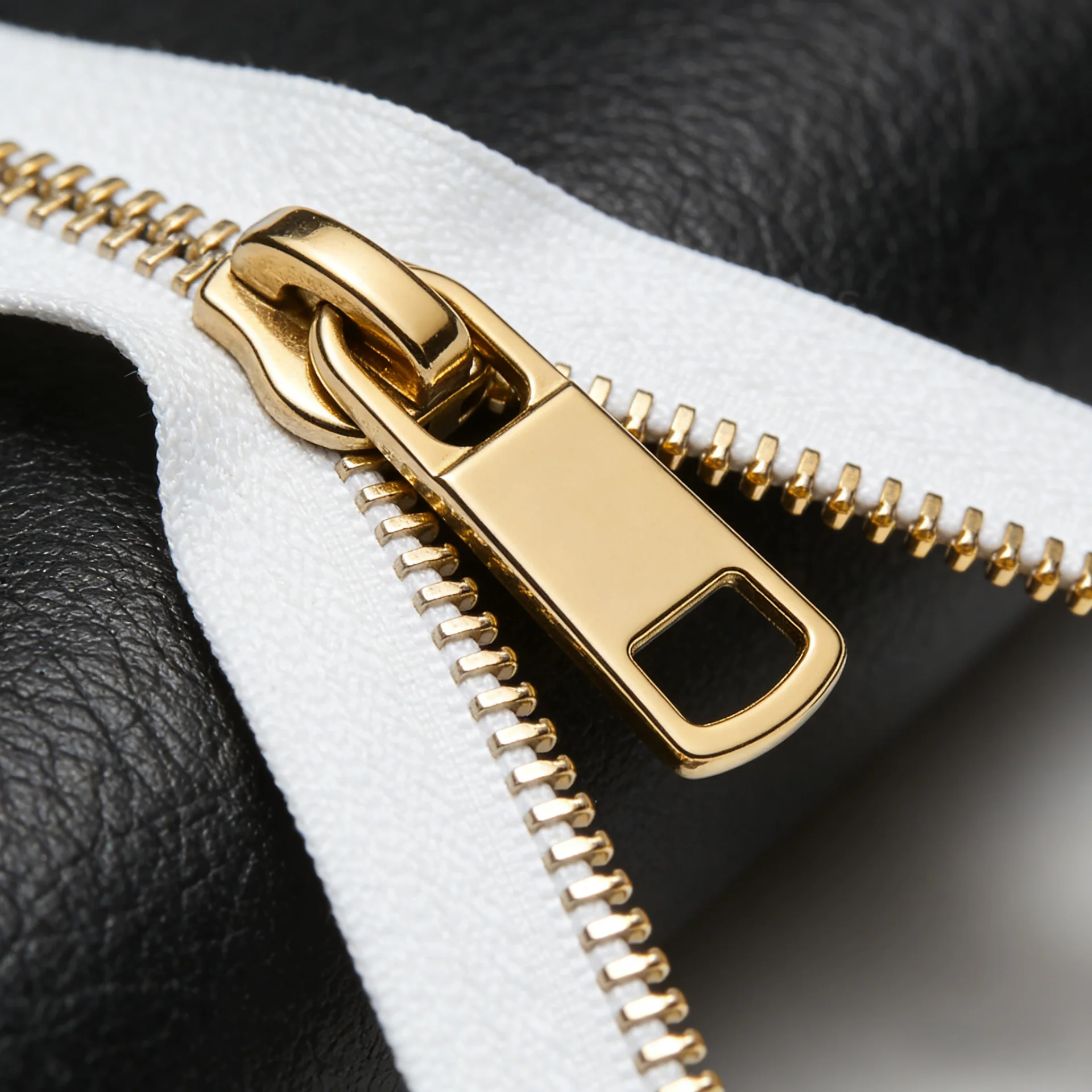 Close-up of a gold zipper on black leather with white fabric, highlighting the metal teeth and pull tab.