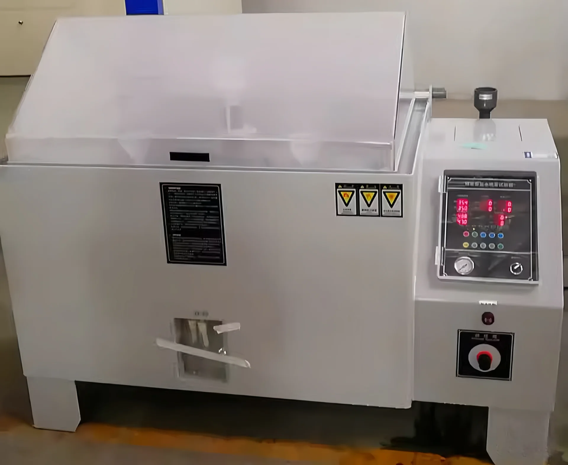 Industrial salt spray tester featuring a control panel with various dials and buttons, used for corrosion testing.