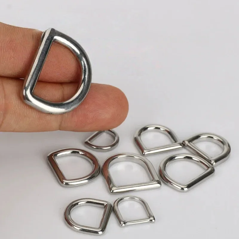 Hand holding a shiny silver metal D-ring among several loose D-rings on a white surface, used in garment and bag accessory applications.
