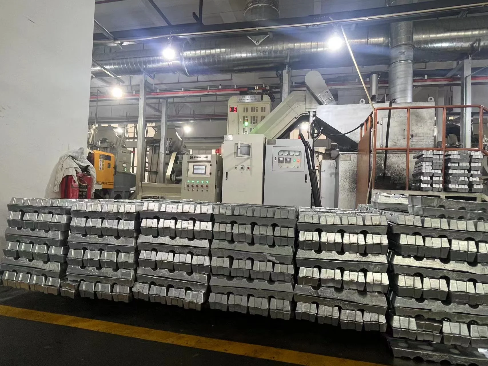 Metal ingots stacked in rows in front of industrial machinery on a factory floor, highlighting manufacturing environment.