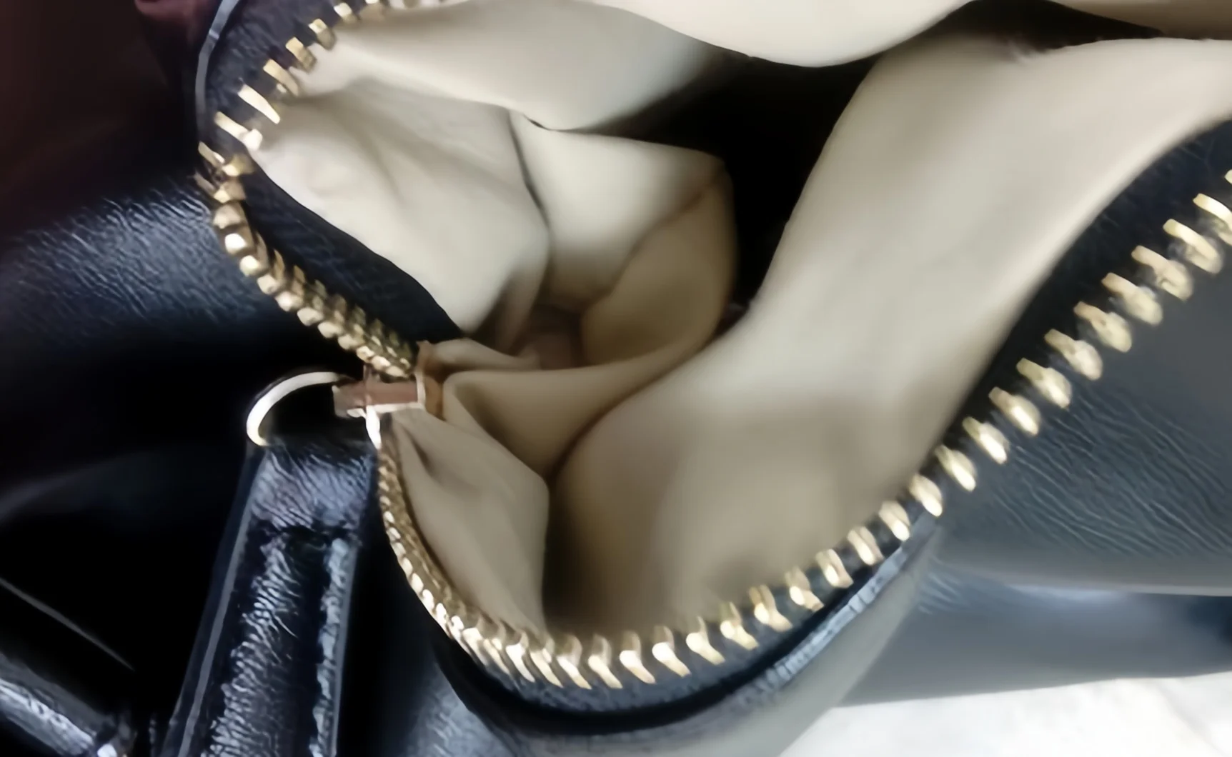 Close-up of an open black leather bag featuring a gold zipper and beige interior lining, highlighting its design and material.