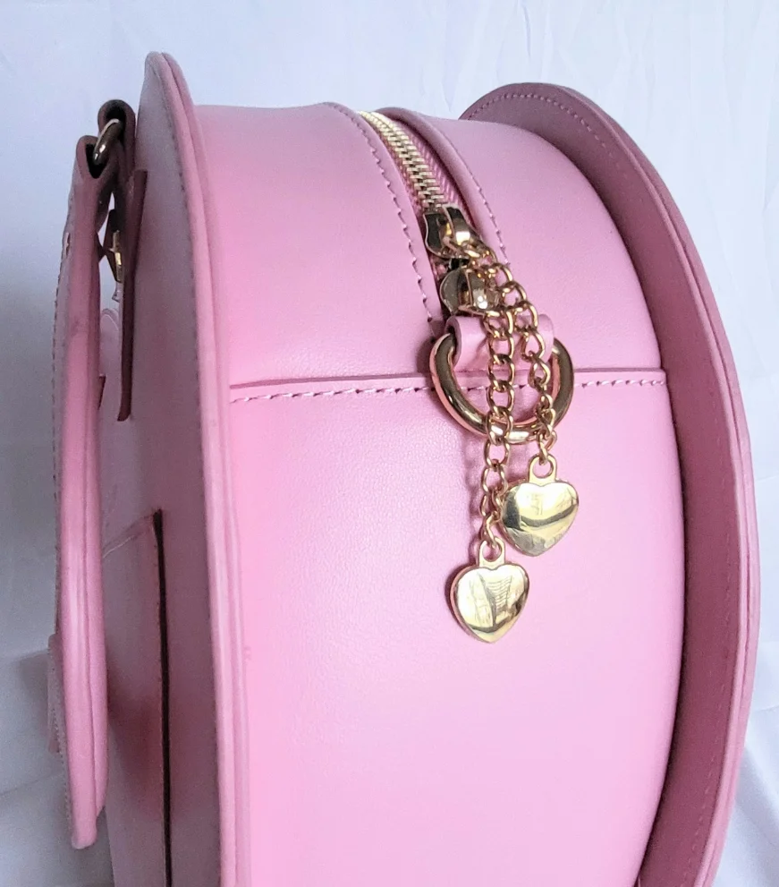 Close-up of a pink round bag featuring a gold zipper and decorative heart-shaped gold chains.