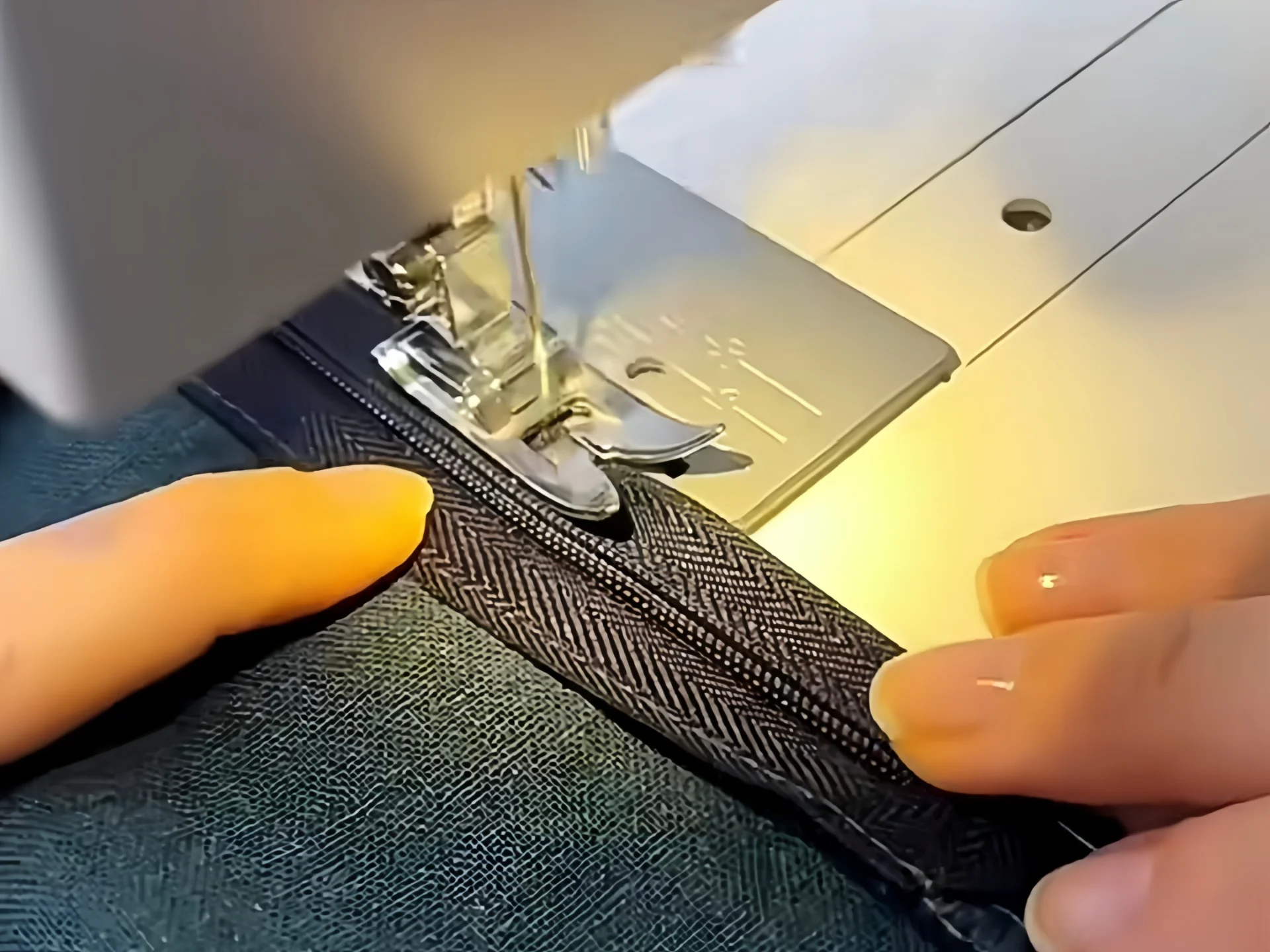 Close-up of hands guiding fabric and zipper under sewing machine needle, showcasing precision sewing techniques.