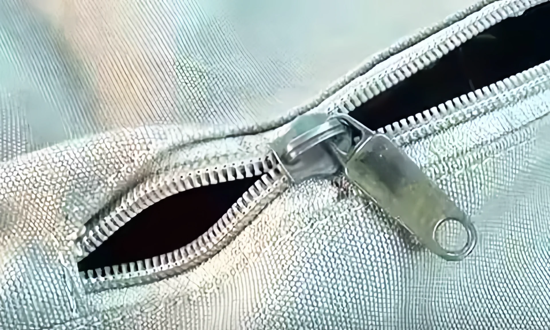 Close-up of a textured metal zipper partially opened on a fabric bag with intricate patterning.