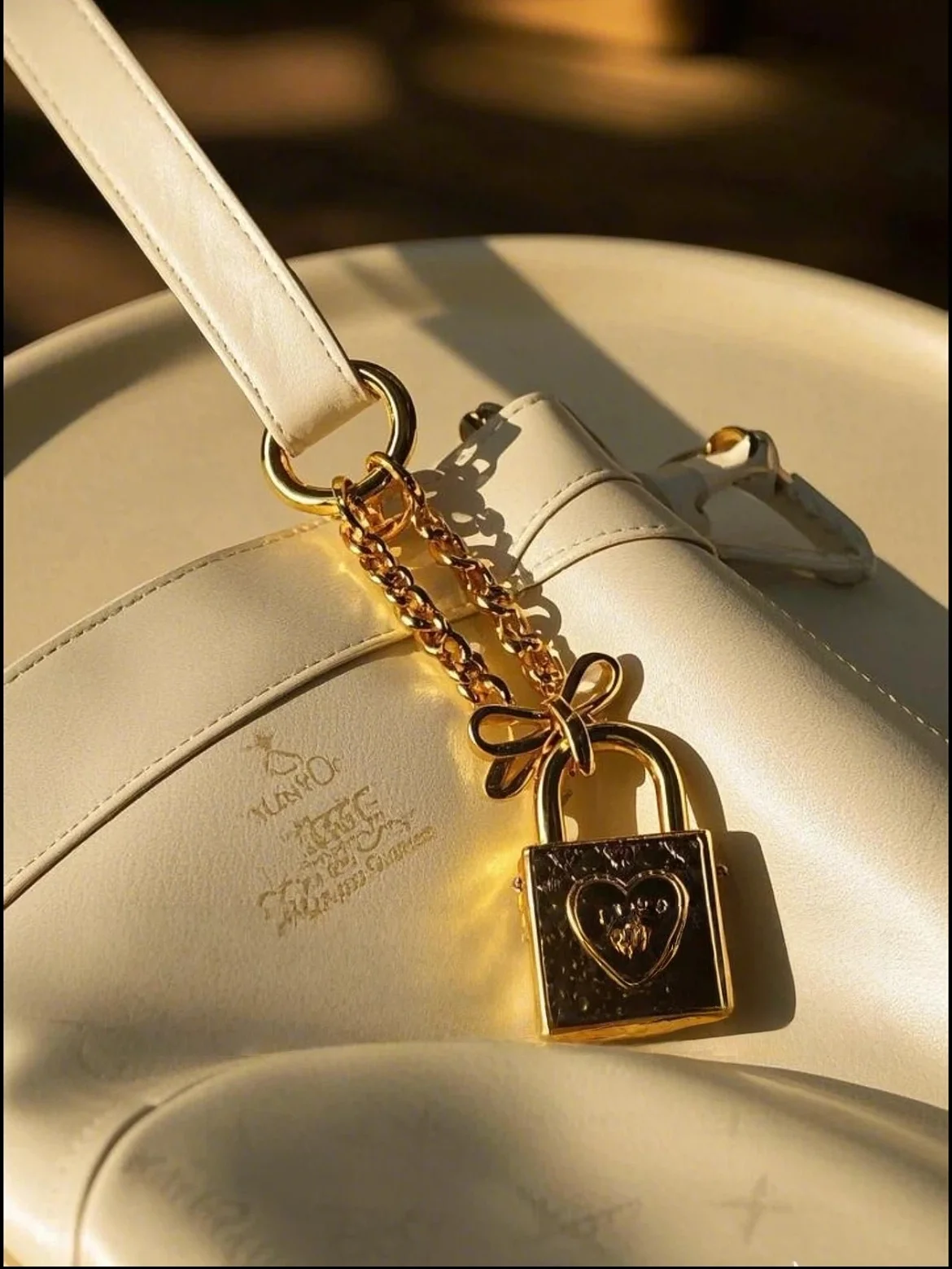 White leather bag with a gold chain and heart-shaped lock charm, casting a shadow in warm sunlight.