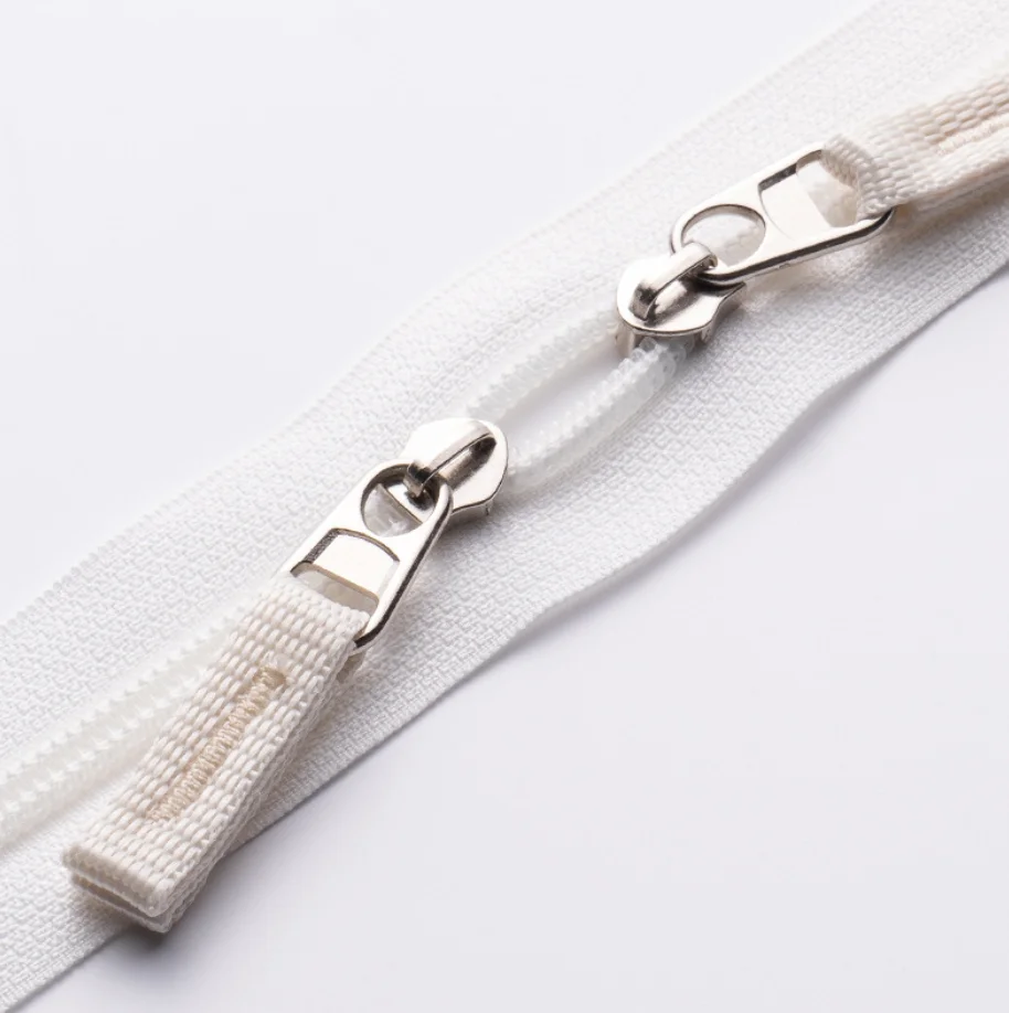 Close-up of a white zipper with metallic pullers on fabric, showing detailed texture and design.
