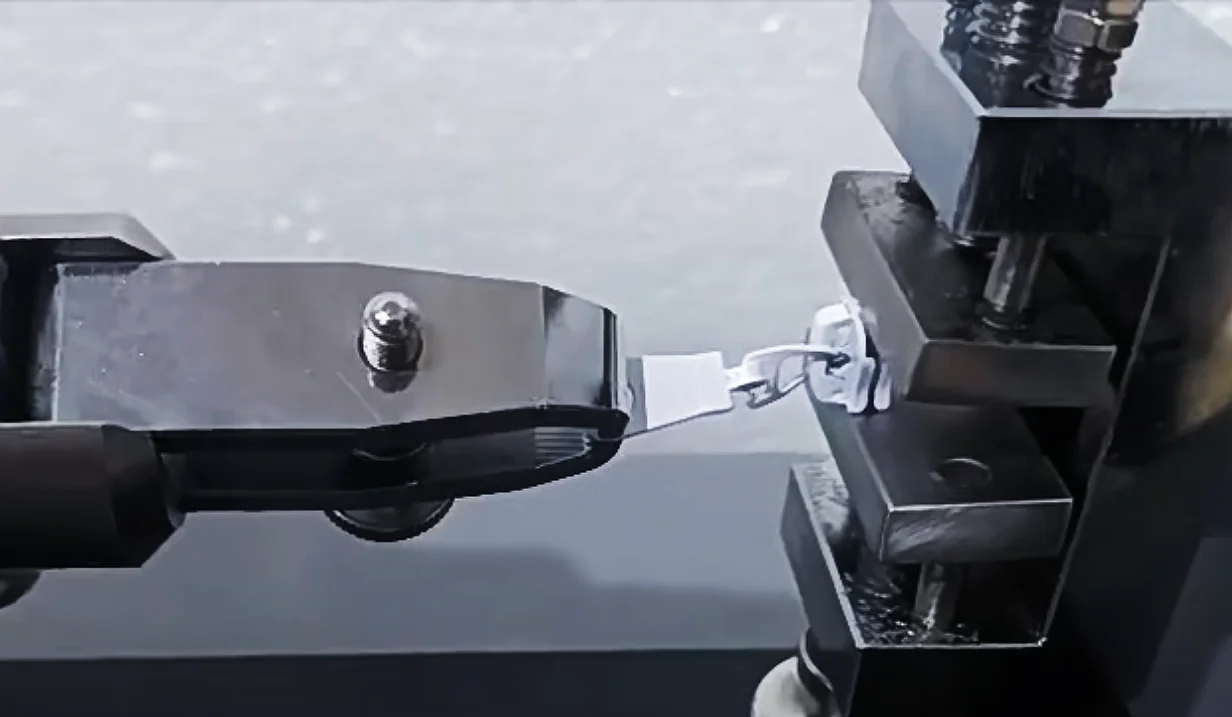 A close-up view of a machine testing the strength of a zipper, with clamps holding the fabric in place.