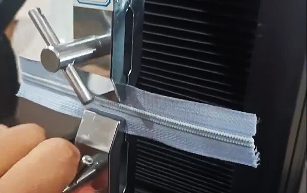 Person using a machine to test the tensile strength of a zipper by holding it between metal clamps.