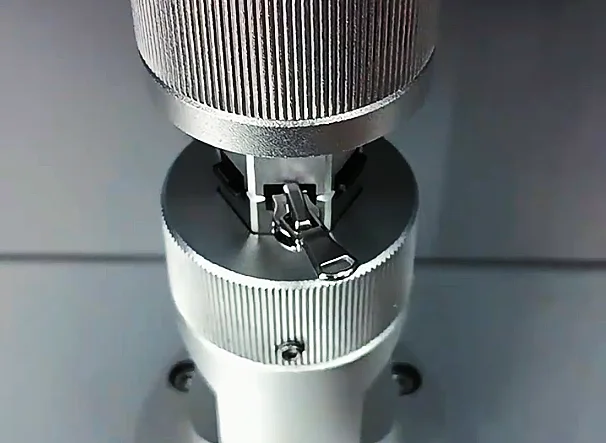 Close-up of a zipper being tested on a professional industrial machine to assess its durability and performance.
