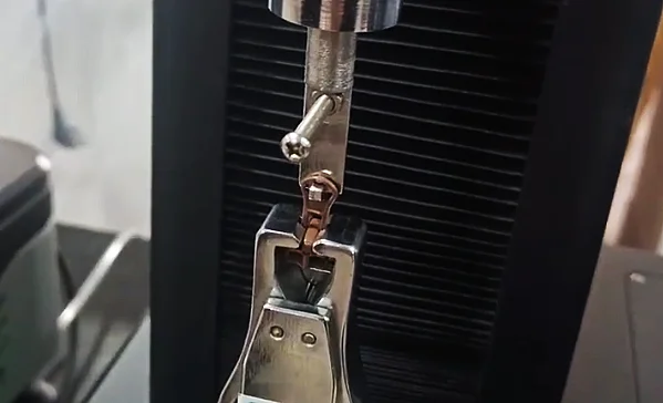 Close-up of a zipper being tested in a tension testing machine, highlighting the precision and durability assessment in garment accessories.